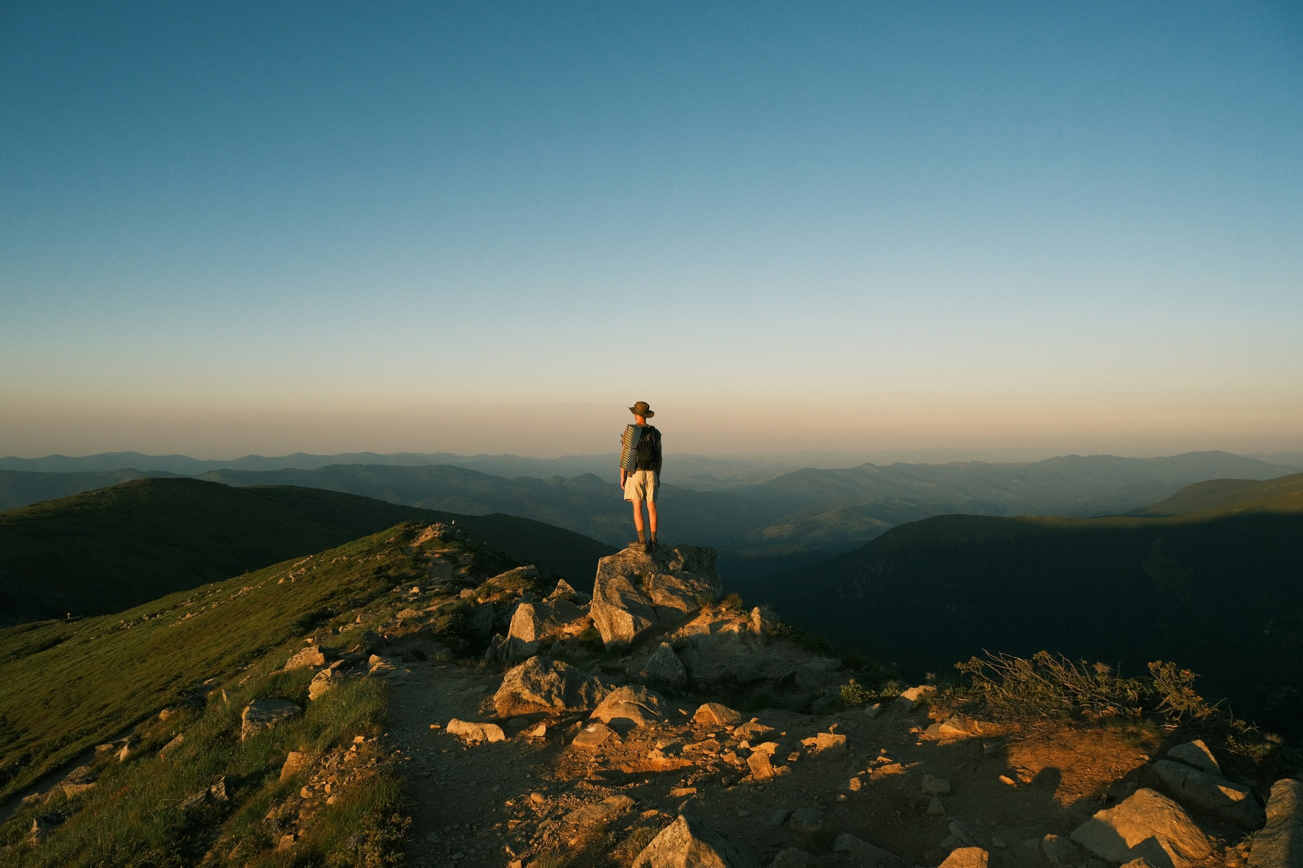 A hiker standing on a rocky ridge overlooking hazy mountains at dusk